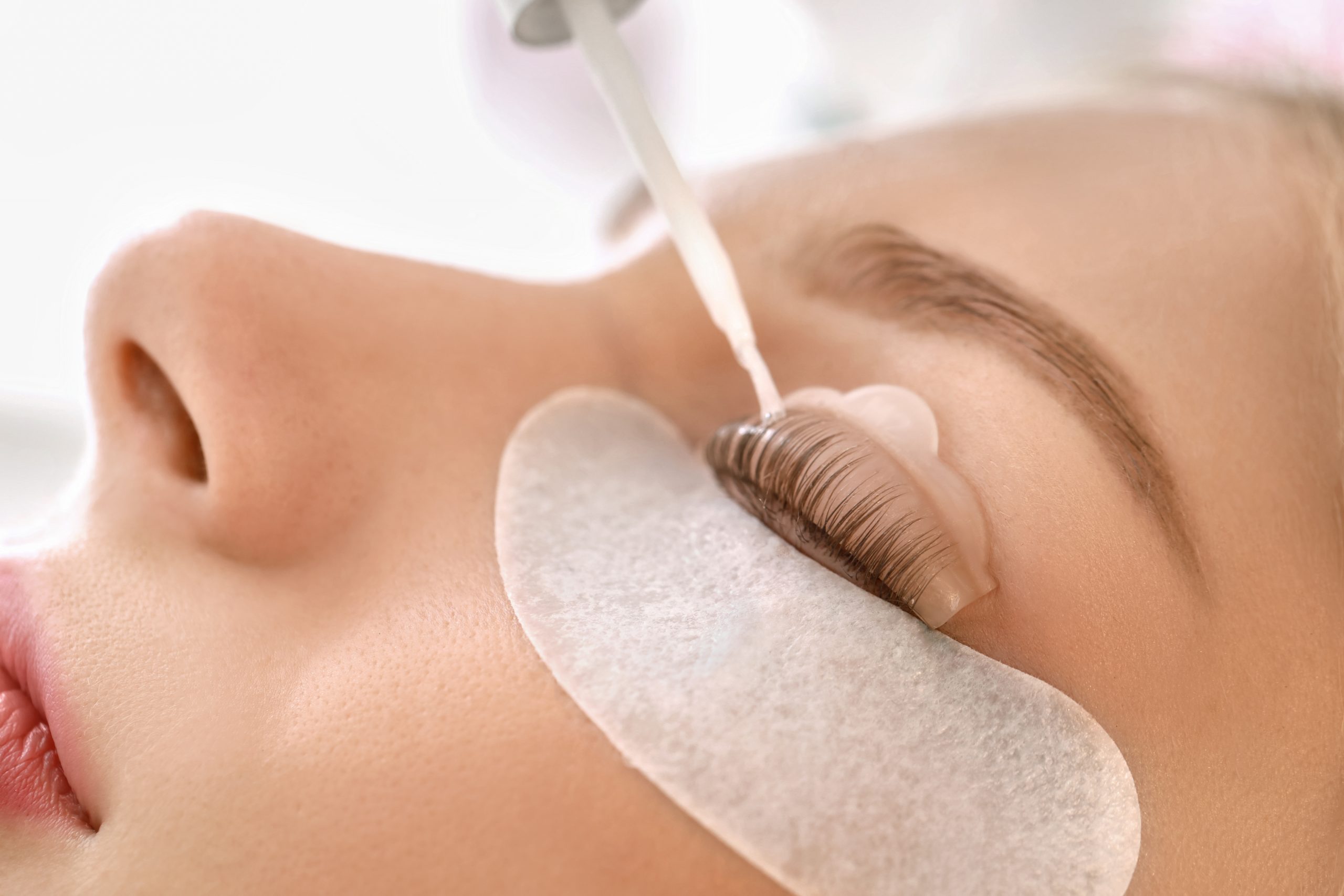Young woman undergoing procedure of eyelashes lamination in beau